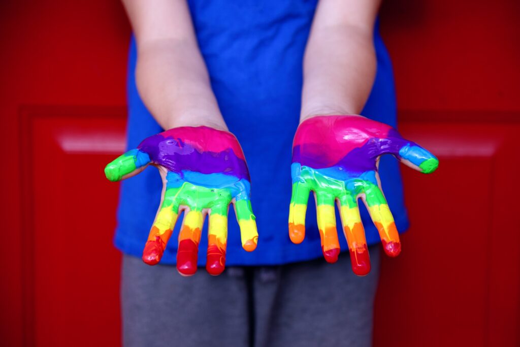 Le manu di un bambino ricoperte con i colori dell'arcobaleno