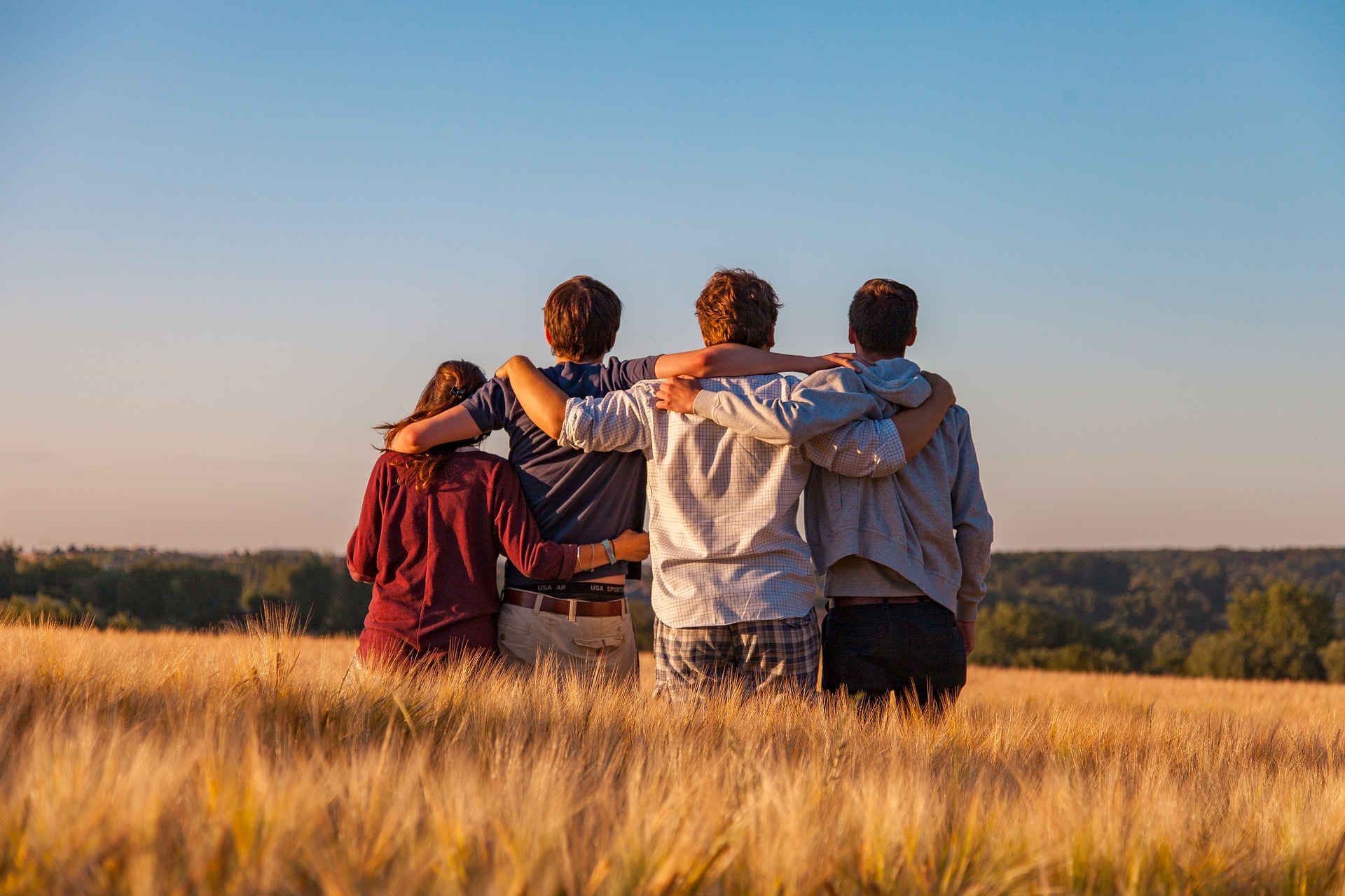 Un gruppo di adolescenti di spalle, abbracciati in un campo di grano