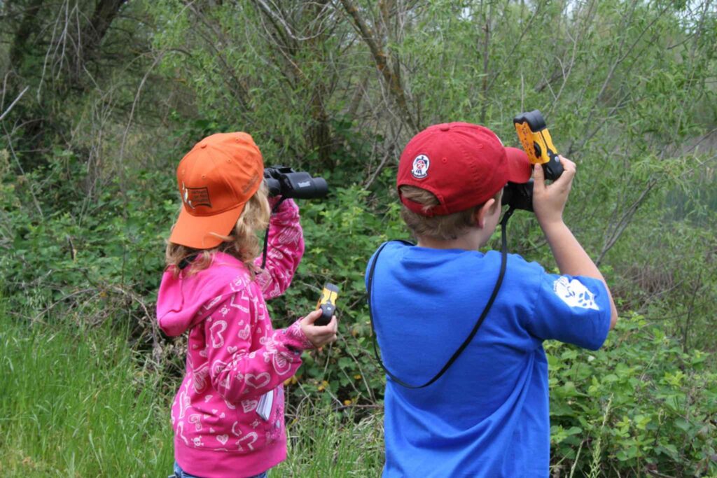 Due bambini di spalle, nella natura, osservano con dei cannocchiali