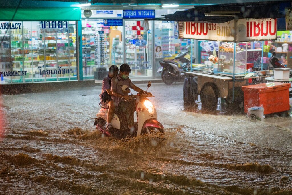 Due ragazzi su uno scooter, in mezzo a un nubifragio, in una città asiatica