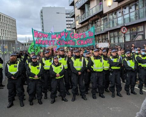 Glasgow, 3 novembre 2021. La polizia blocca la marcia di Extinction Rebellion che si dirigeva nei paraggi della Cop26. Lo striscione gioca sul doppio senso della parola "cop", in inglese poliziotto: quante cop (e quanti "cops") ci vogliono per arrestare il cambiamento climatico?