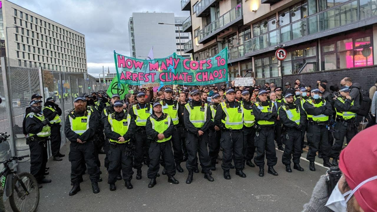 Glasgow, 3 novembre 2021. La polizia blocca la marcia di Extinction Rebellion che si dirigeva nei paraggi della Cop26. Lo striscione gioca sul doppio senso della parola "cop", in inglese poliziotto: quante cop (e quanti "cops") ci vogliono per arrestare il cambiamento climatico?