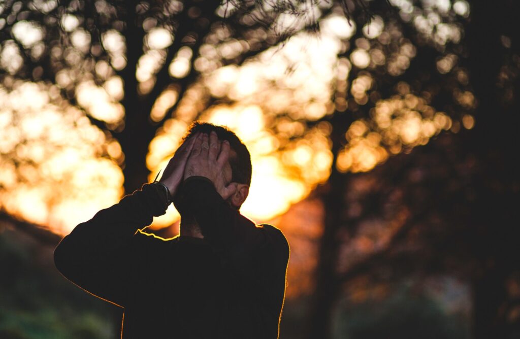 Un uomo si copre il volto con le mani. Sullo sfondo, un paesaggio naturale al tramonto