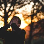 Un uomo si copre il volto con le mani. Sullo sfondo, un paesaggio naturale al tramonto