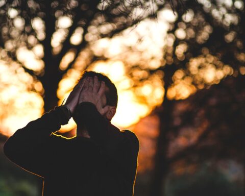 Un uomo si copre il volto con le mani. Sullo sfondo, un paesaggio naturale al tramonto