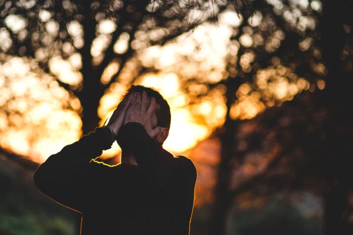 Un uomo si copre il volto con le mani. Sullo sfondo, un paesaggio naturale al tramonto