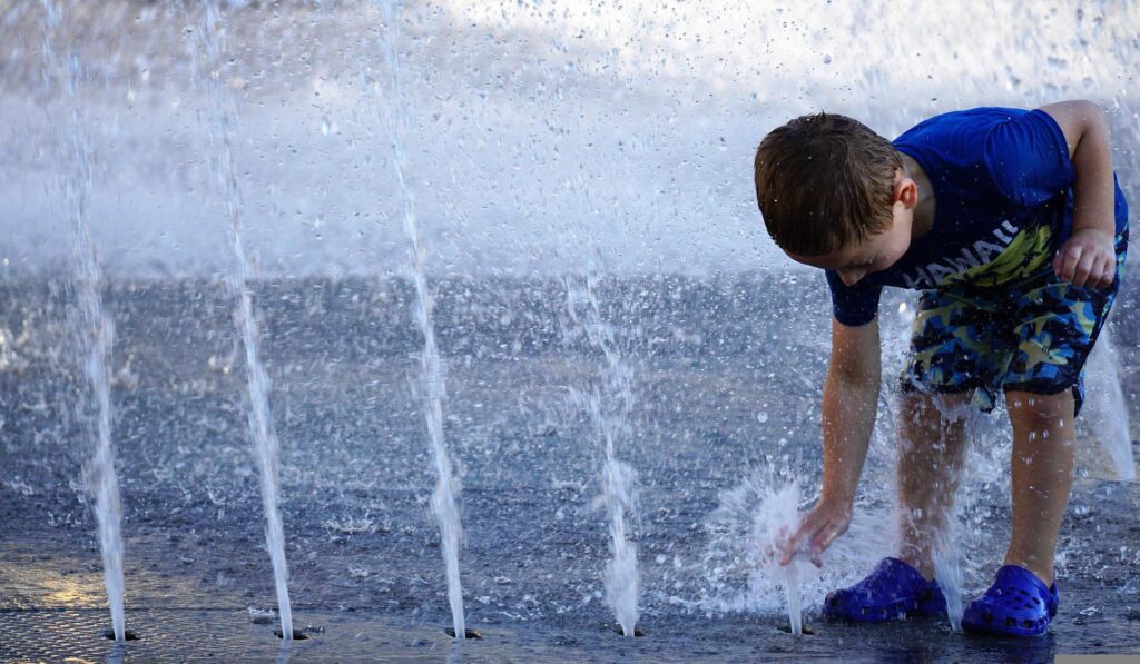 Un bambino cerca di rinfrescarsi in una fontana cittadina