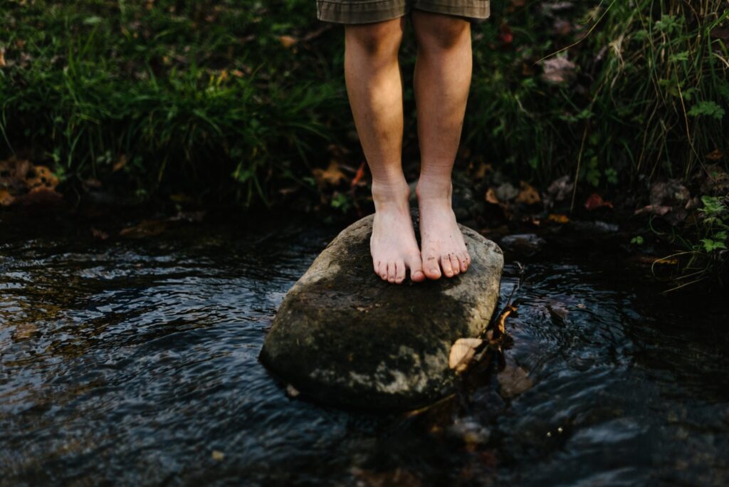 Gambe di un bambino su un sasso in mezzo ad un fiume o torrente