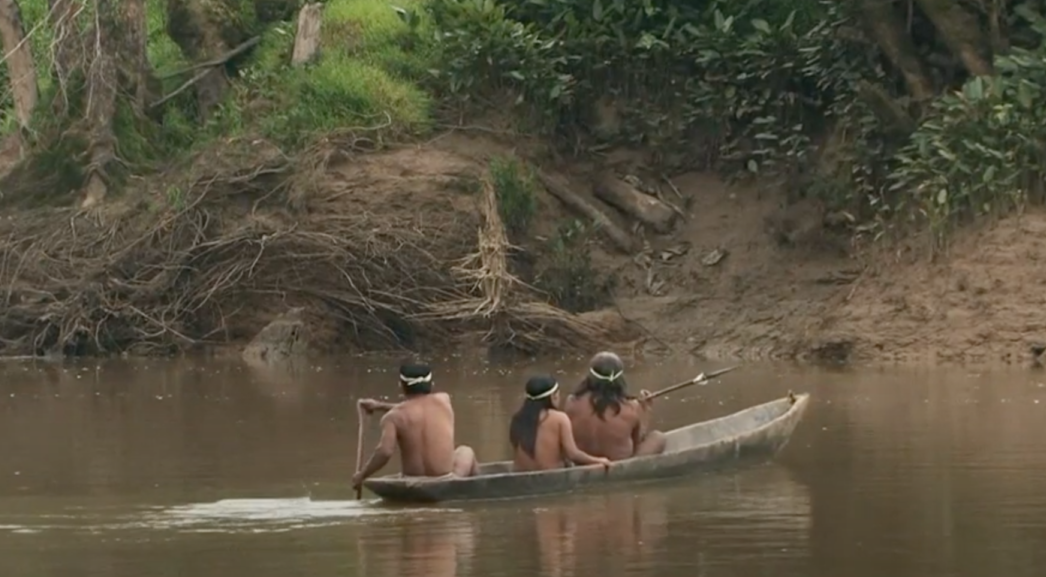 Tre indigeni amazzonici di spalle mentre attraversano un fiume su una imbarcazione