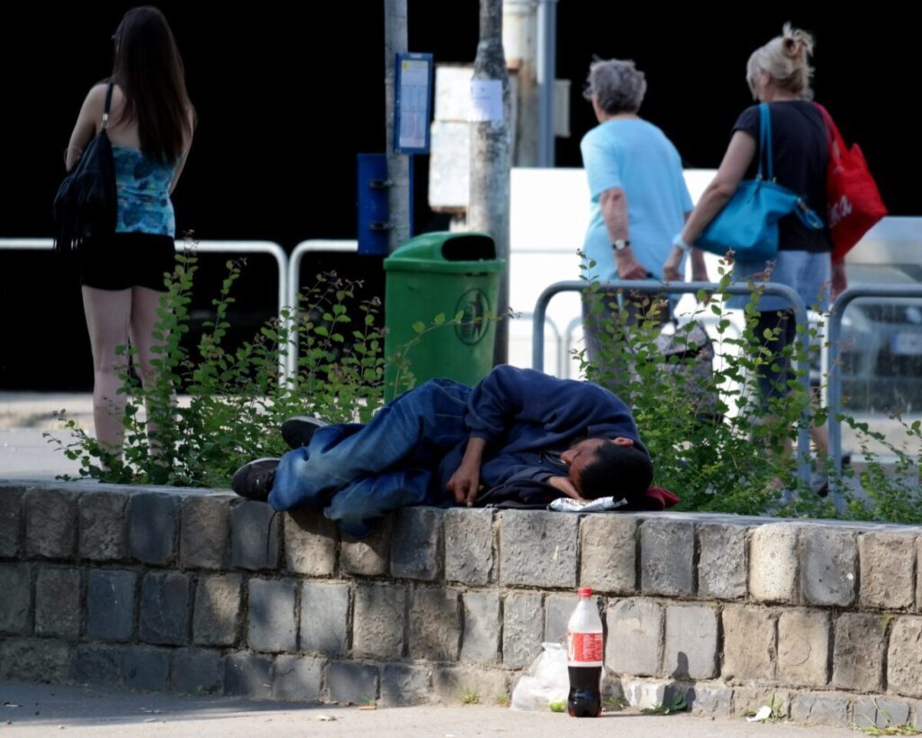 Un uomo, probabilmente senza fissa dimora, dorme per strada su un muretto