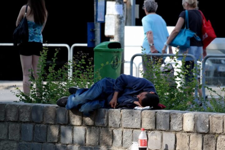 Un uomo, probabilmente senza fissa dimora, dorme per strada su un muretto