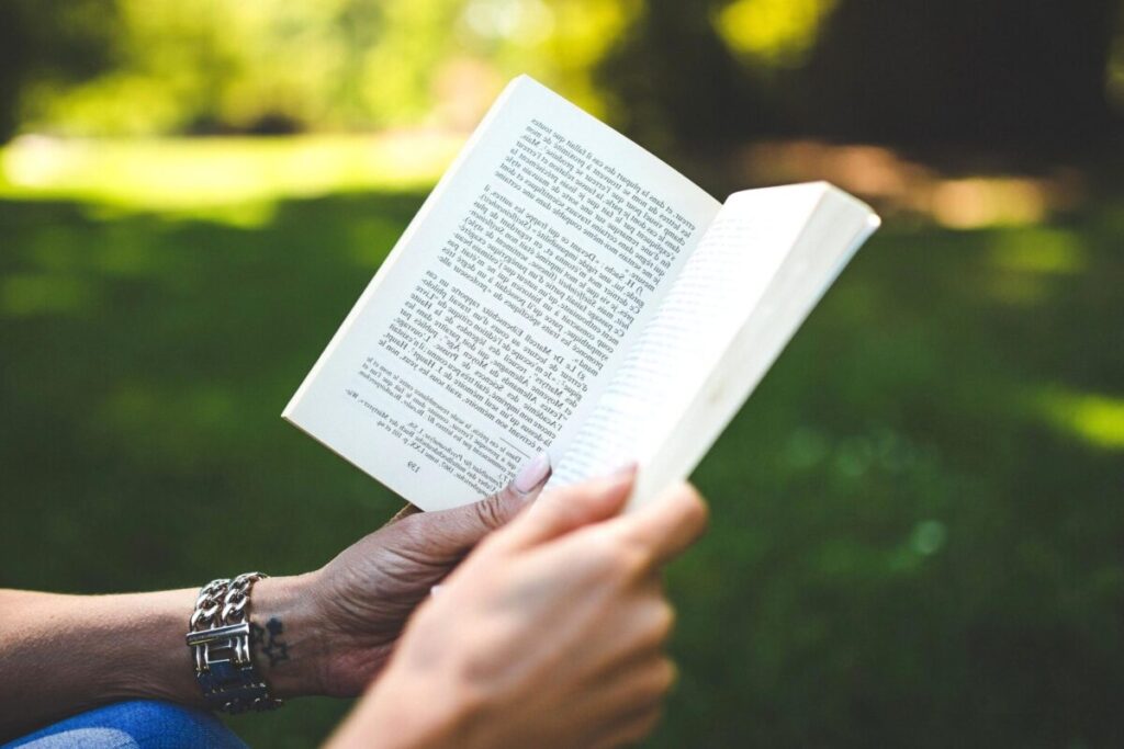 Due mani di persone diverse sfogliano un libro nella natura