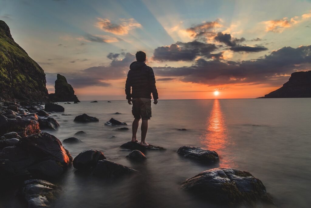 Un uomo di spalle guarda il mare da un punto roccioso