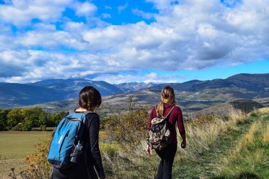 Due viaggiatrici camminano nella campagna con gli zaini sulle spalle