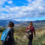 Due viaggiatrici camminano nella campagna con gli zaini sulle spalle