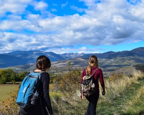 Due viaggiatrici camminano nella campagna con gli zaini sulle spalle