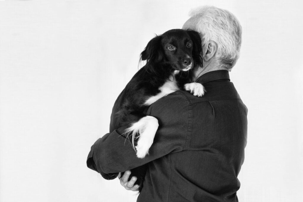 Un uomo anziano di spalle, tiene in braccio un bellissimo cane meticcio bianco e nero