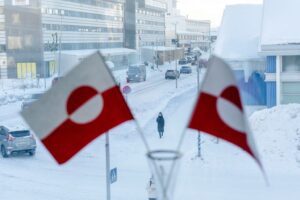 Groenlandia, il futuro è adesso: una donna cammina sulla neve, tra due bandiere nazionali
