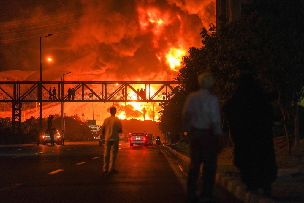 Teheran, Iran. 15 giugno 2025. Gli iraniani, che si guardano come un pennacchio di fumo pesante e fuoco, si alzano da una raffineria di petrolio a Teheran, dopo essere stati colpiti da un attacco israeliano durante la notte, domenica 15 giugno 2025.