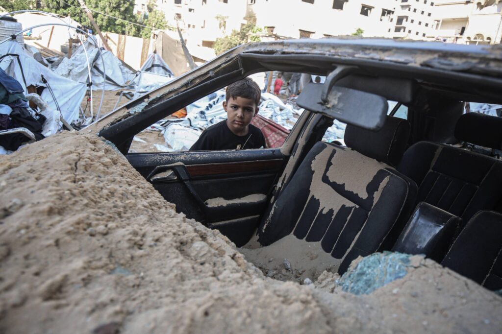 Un bambino davanti un'auto distrutta a Gaza