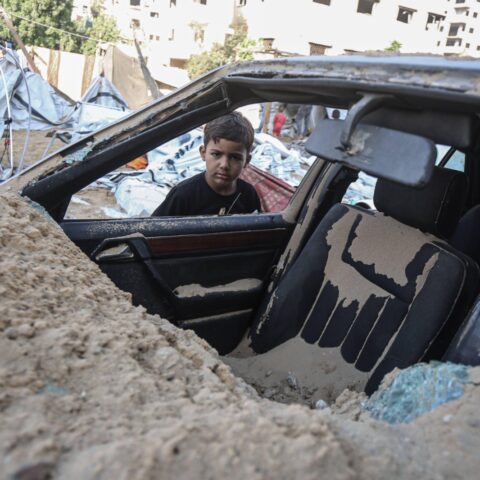 Un bambino davanti un'auto distrutta a Gaza