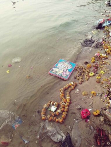 A Varanasi, il fiume sacro reca con sé, tra i rifiuti, un quadro raffigurante gli Dei Visnù e Laksmi.