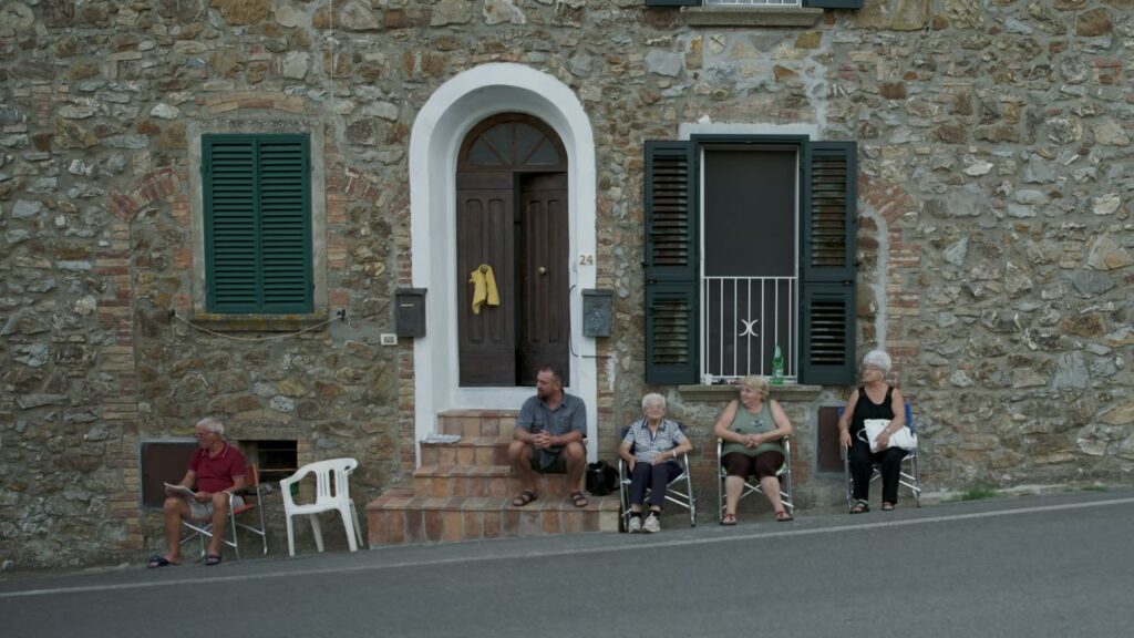 Tatti, il paese dei sognatori: una casa di pietra lungo la strada con alcune persone sedute ad aspettare