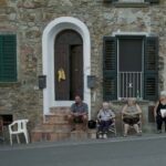 Tatti, il paese dei sognatori: una casa di pietra lungo la strada con alcune persone sedute ad aspettare