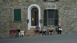 Tatti, il paese dei sognatori: una casa di pietra lungo la strada con alcune persone sedute ad aspettare