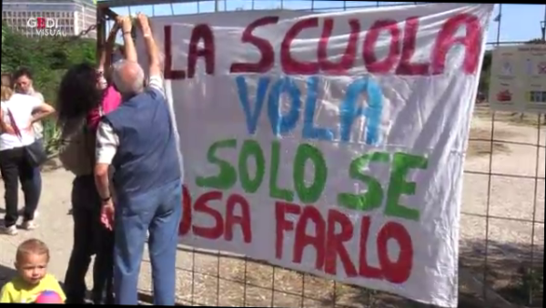 Un gruppo di insegnanti tiene uno striscione con scritto "La scuola vola solo se osa farlo"