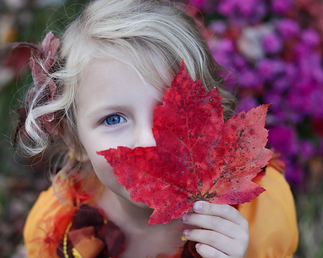 Una bambina ci osserva con una foglia d'autunno sull'occhio sinistro