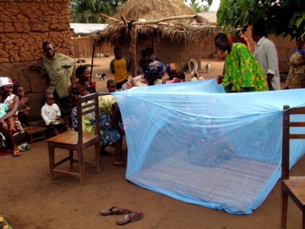 Un uomo in un villaggio africano mostra come utilizzare correttamente le zanzariere per proteggersi dalla malaria