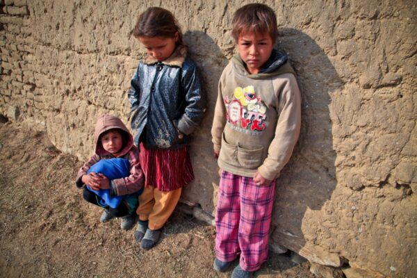 Tre bambini vestiti con abiti rimediati appoggiati ad un muro