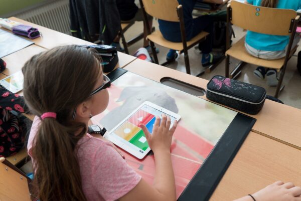 Una bambina con un Ipad, di spalle, in una classe